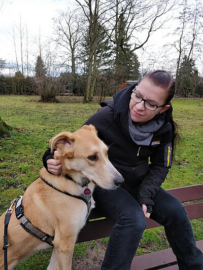 Maria Maria sitzt auf einer Bank und schaut ihren super süßen Hund an.
