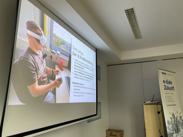Leinwand zeigt Präsenatation mit Bild einer Person mit VR-Brille am Schreibtisch sitzend