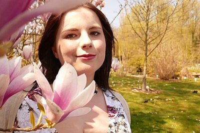 Katinka steht halb hinter einer Blume und lächelt in die Kamera.