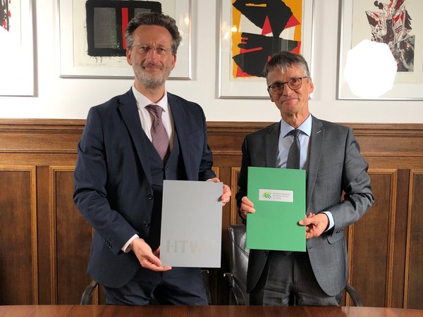 Prof. Dr.-Ing Jean-Alexander Müller (li.) und Prof. Dr. Hans-Joachim Knölker nach der Unterzeichnung des Kooperationsvertrages. (Foto: SAW/HTWK Leipzig) zwei Herren im Anzug halten festliche Mappen in die Kamera