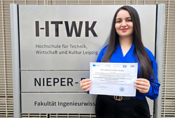 eine Frau steht vor dem Schild des Nieper-Baus der HTWK Leipzig und hält einen Zettel in der Hand